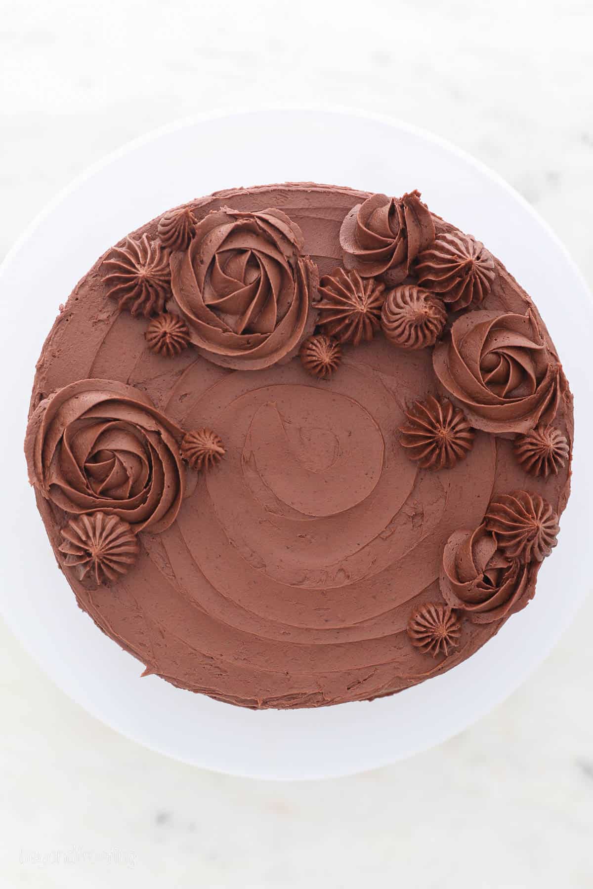 Overhead view of a frosted marble cake partially decorated with chocolate buttercream roses and smaller piped swirls.