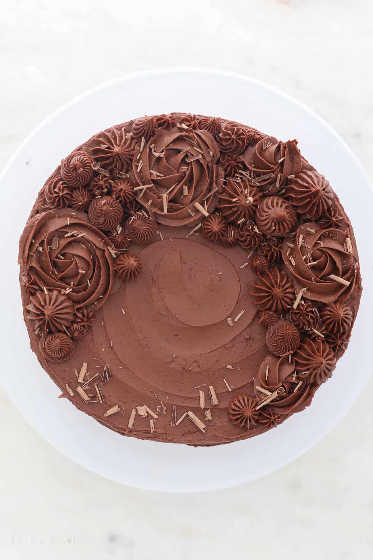 Overhead view of a frosted marble cake decorated with piped chocolate buttercream roses, swirls, and shaved chocolate.