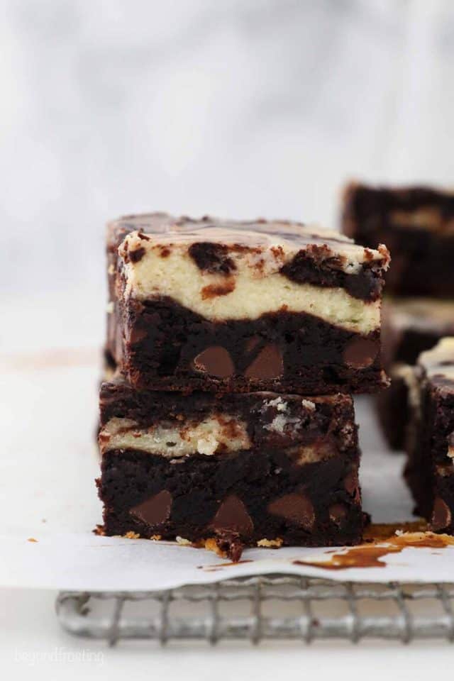 Two cheesecake brownies stacked on a lined wire rack.