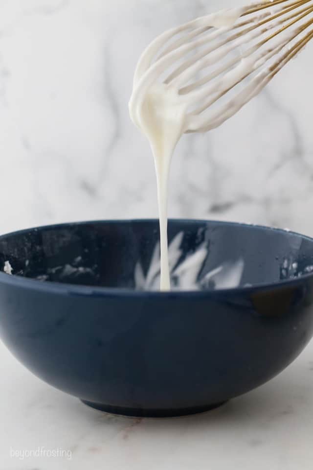 Vanilla glaze dripping of a whisk into a blue bowl