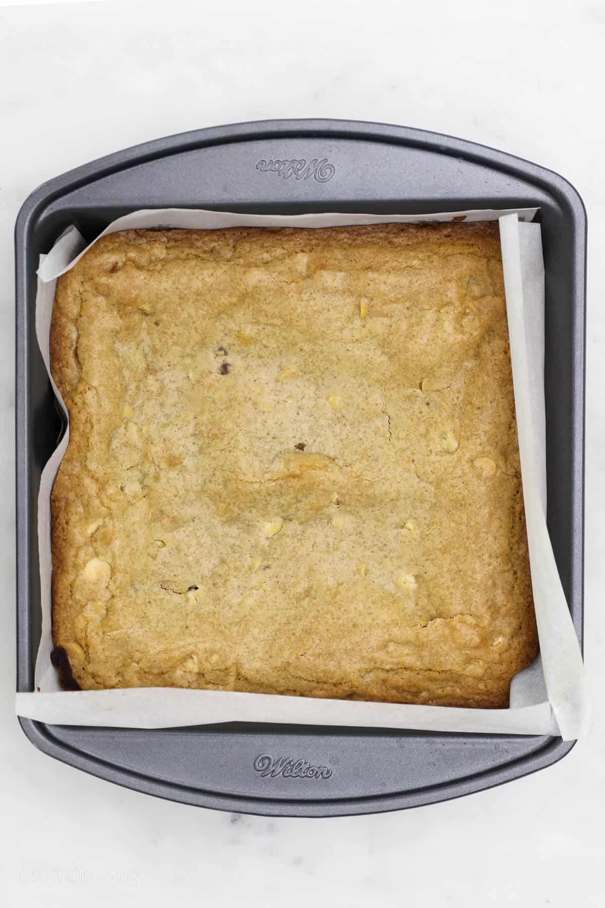 Baked blondies in a parchment-lined cake pan.