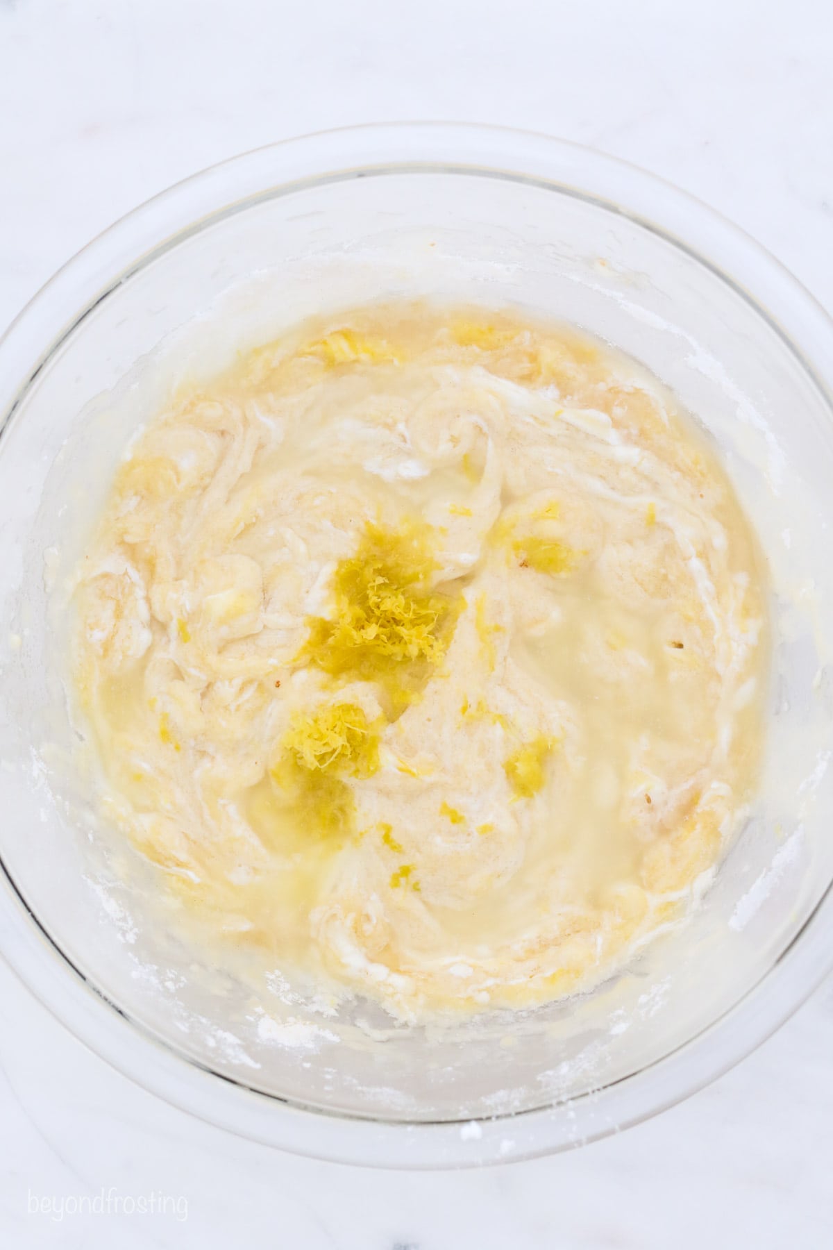 Lemon zest added to lemon bread batter in a glass mixing bowl.