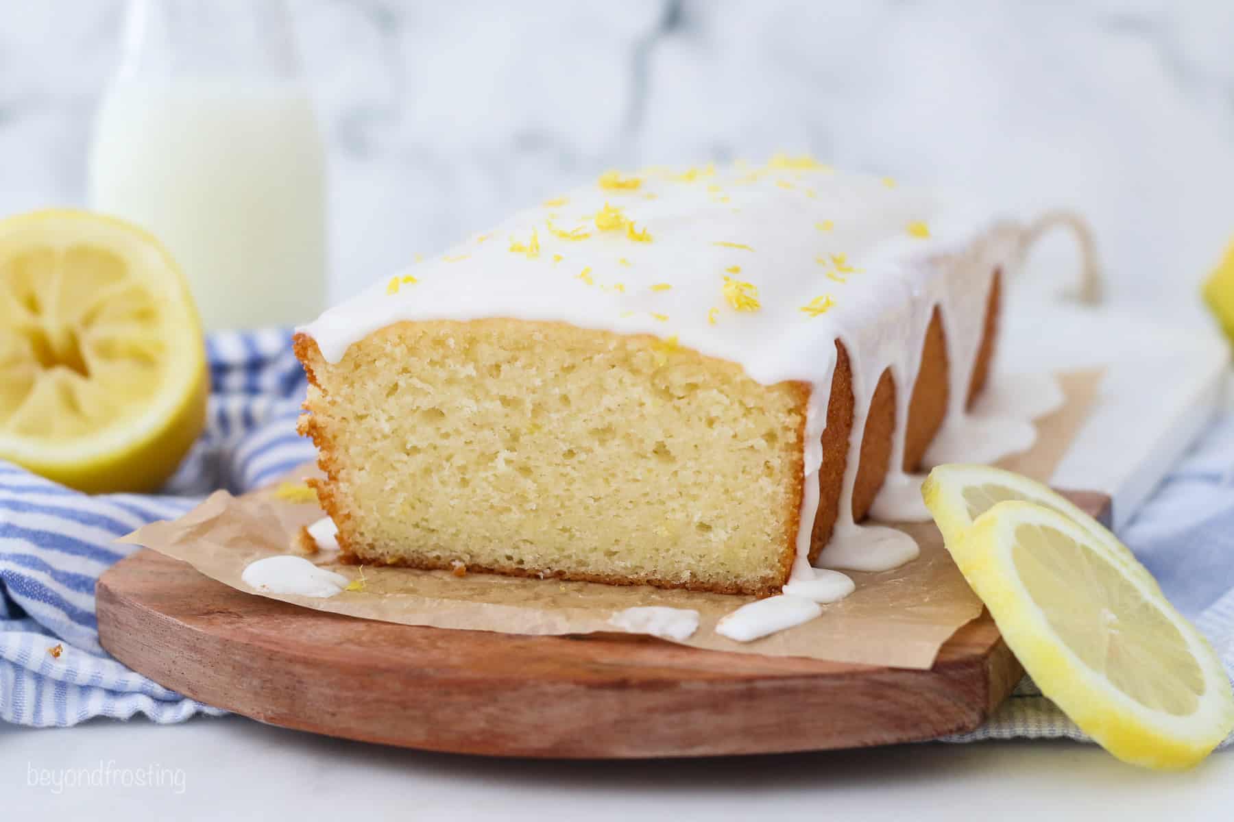 Glazed lemon bread on a wooden cutting board lined with parchment paper, next to a lemon slice.