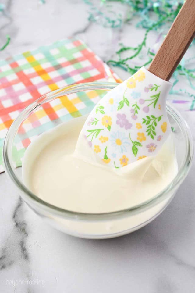 A glass bowl with melted white chocolate and a spatula