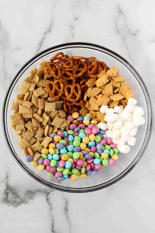 overhead of glass bowl with mixture of pretzels, Chex cereal, mini marshmallows, M&Ms, and little bunny grahams