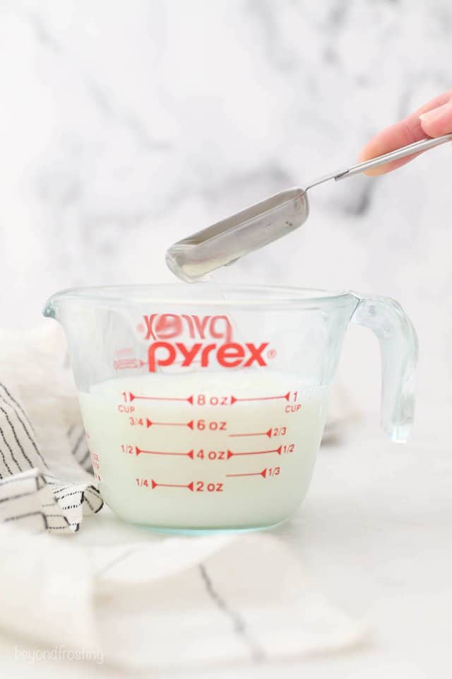 A Tablespoon of Fresh Lemon Juice Being Poured Into a Pyrex Measuring Cup Filled with Milk
