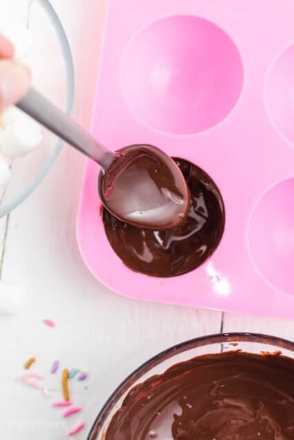 A spoon dropping chocolate into a silicone mold