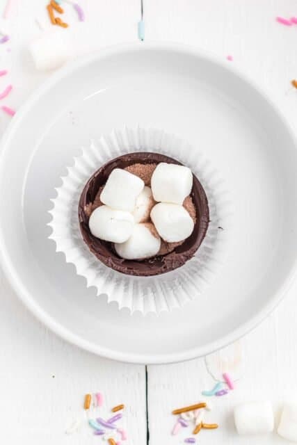 half of a hot chocolate bomb sitting in a cupcake wrapper filled with marshmallows