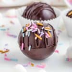 two hot chocolate bombs on a white table, garnished with sprinkles