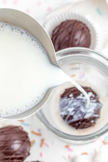 milk being poured into a cup over top of a hot chocolate bomb