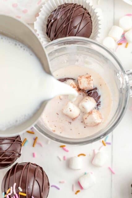 milk being poured into a cup over top of a hot chocolate bomb with marshmallows