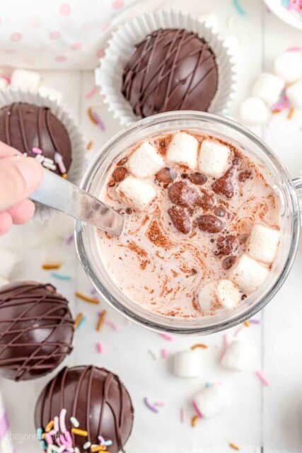 a spoon stirring a cup of hot chocolate with marshmallows