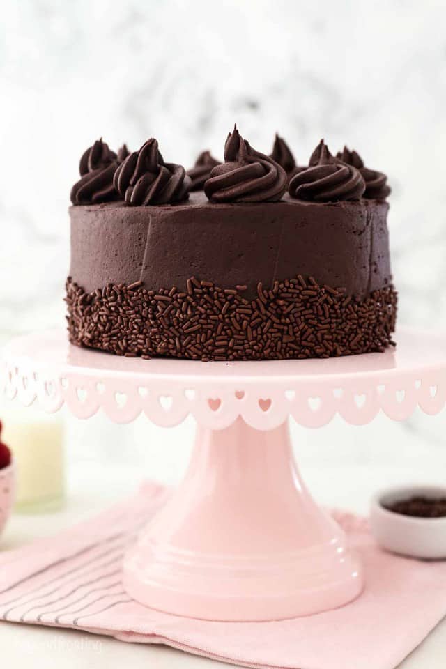 A Small Frosted and Decorated Chocolate Cake on Top of a Pink Cake Stand