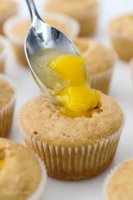 A spoon dropping chopped peaches into the center of a cupcake