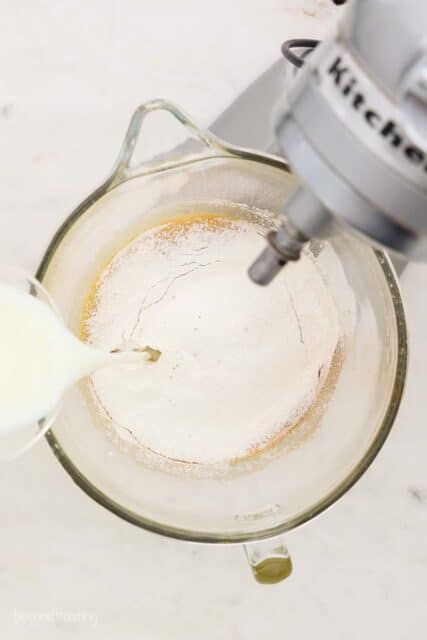 overhead of a stand mixer with flour in the bow and milk pouring in