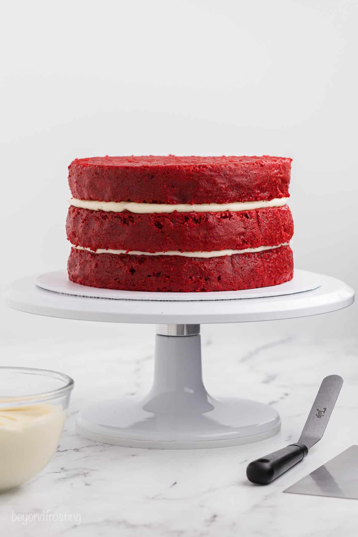 Assembled red velvet layer cake on a cake stand.