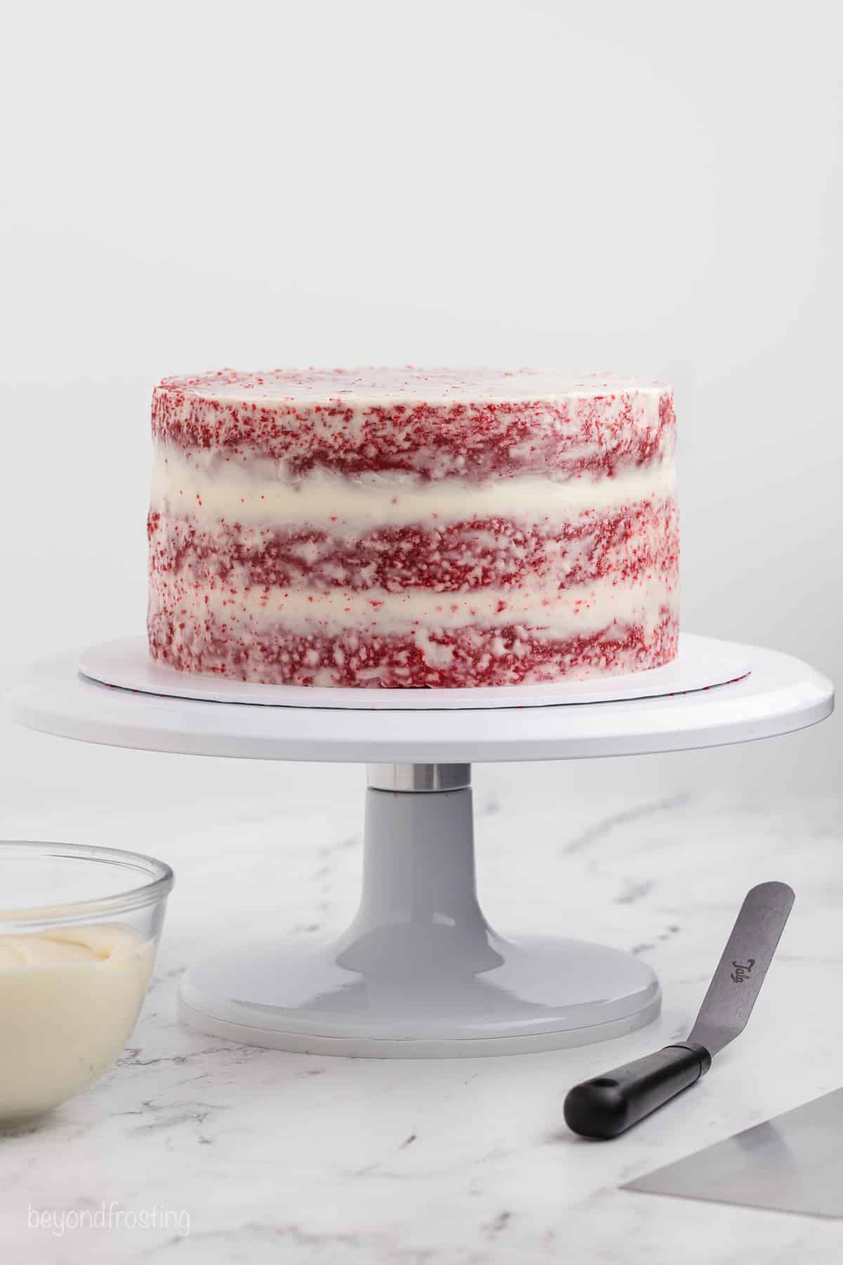 Red velvet layer cake with a crumb coat on a cake stand.