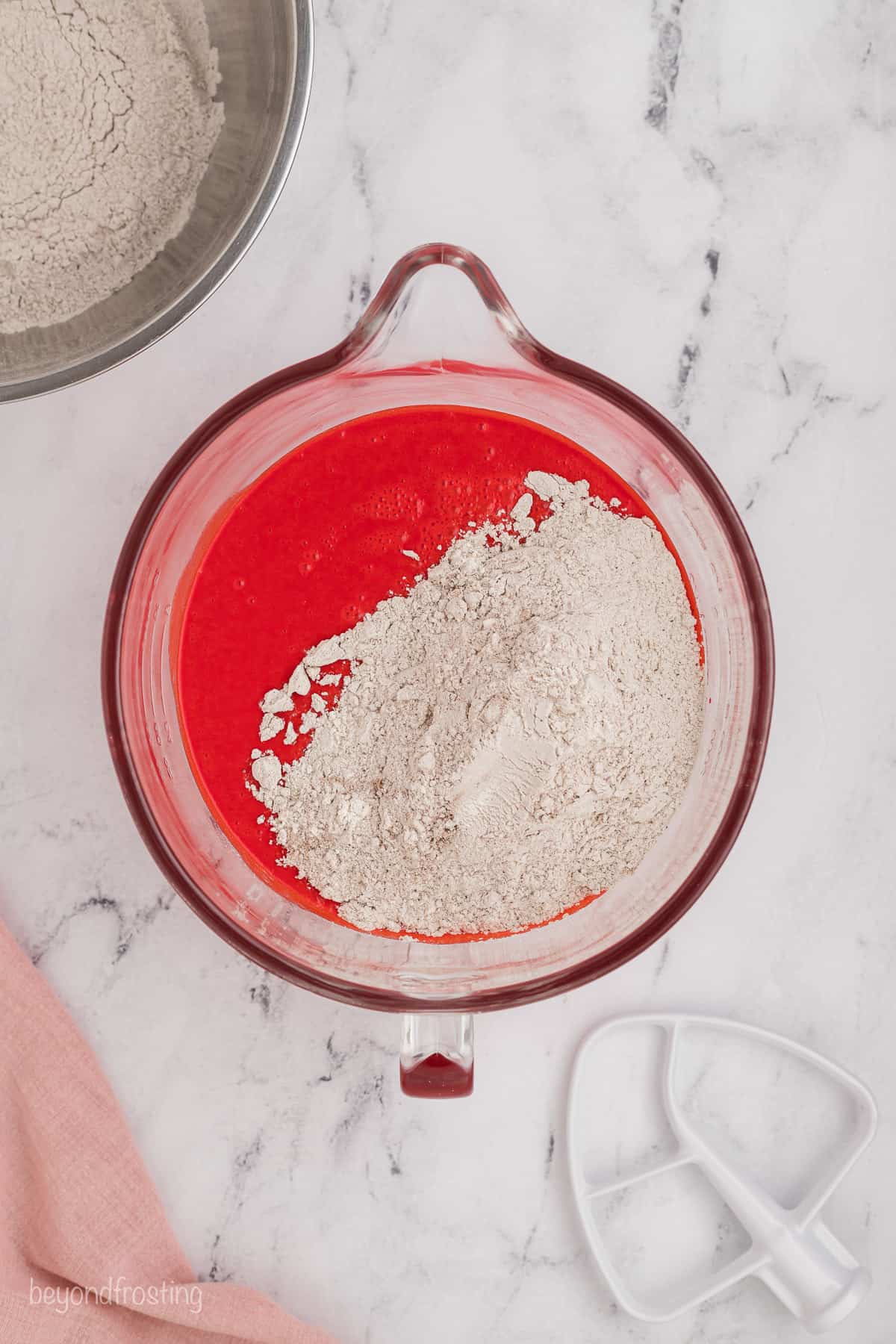 Flour added to red velvet cake batter in a glass mixing bowl.
