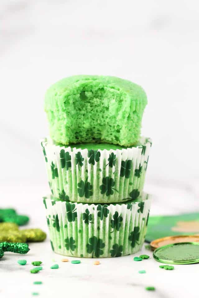 Three green cupcakes stacked on top of one another with shamrock cupcake wrappers