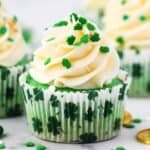 A green colored cupcake frosted and decorated with shamrock sprinkles