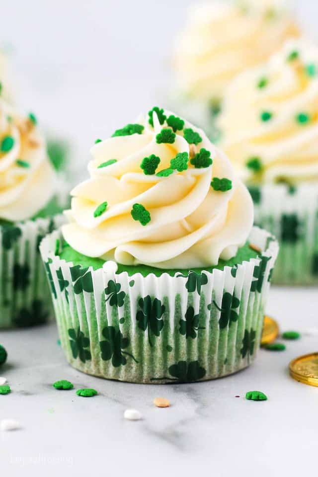 A green colored cupcake frosted and decorated with shamrock sprinkles