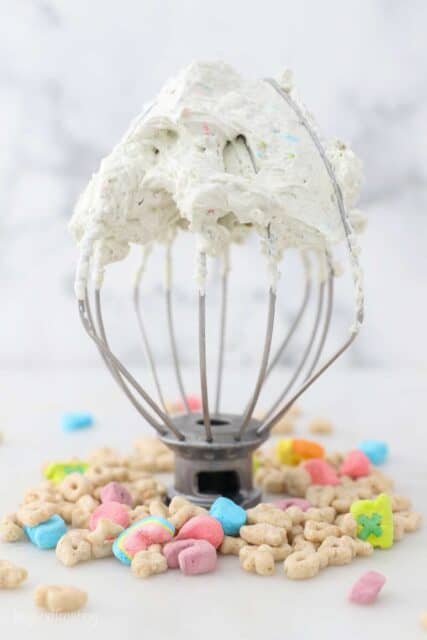 a wire whisk with whipped cream surrounded by Lucky Charms Cereal