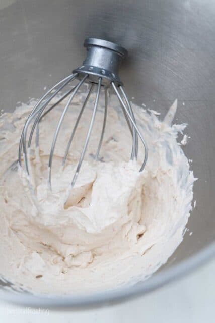 a wire whisk inside a metal mixing bowl with whipped cream