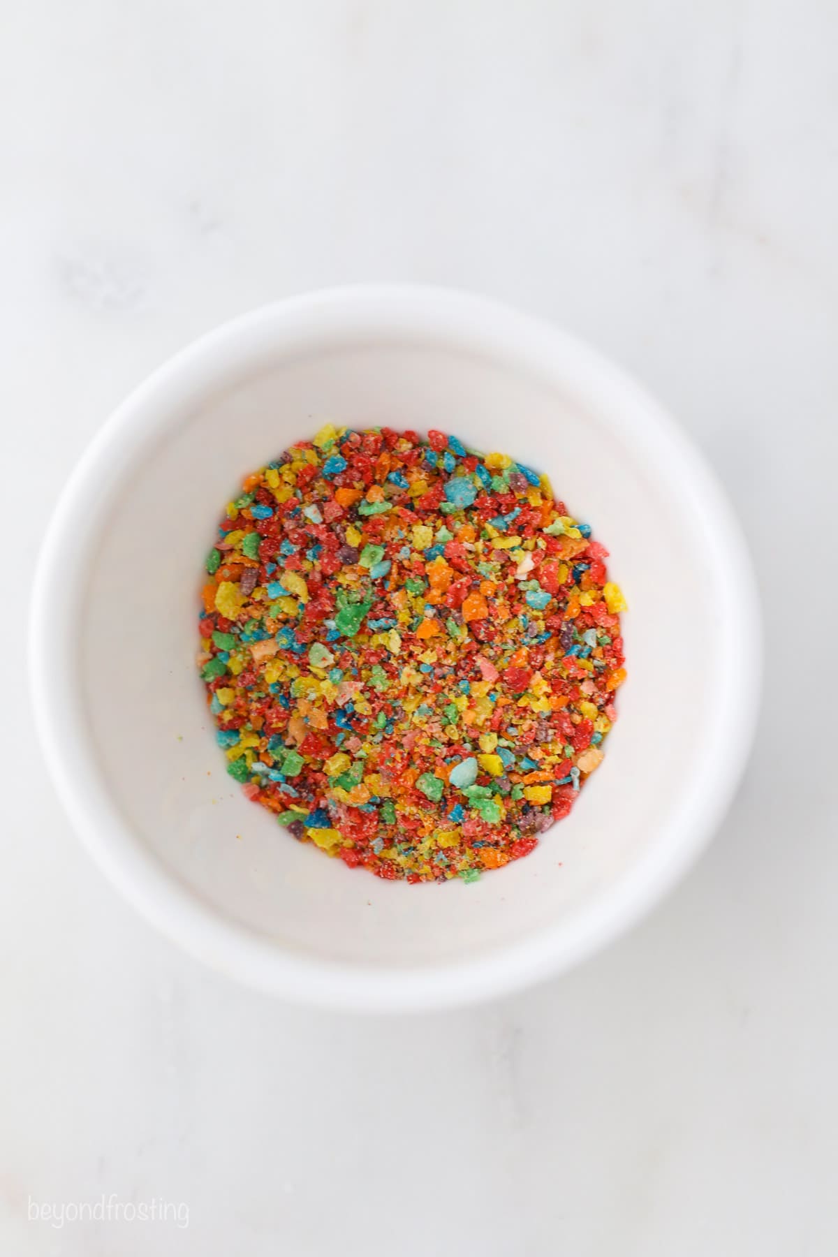 Overhead view of dry Fruity Pebbles cereal in a bowl.
