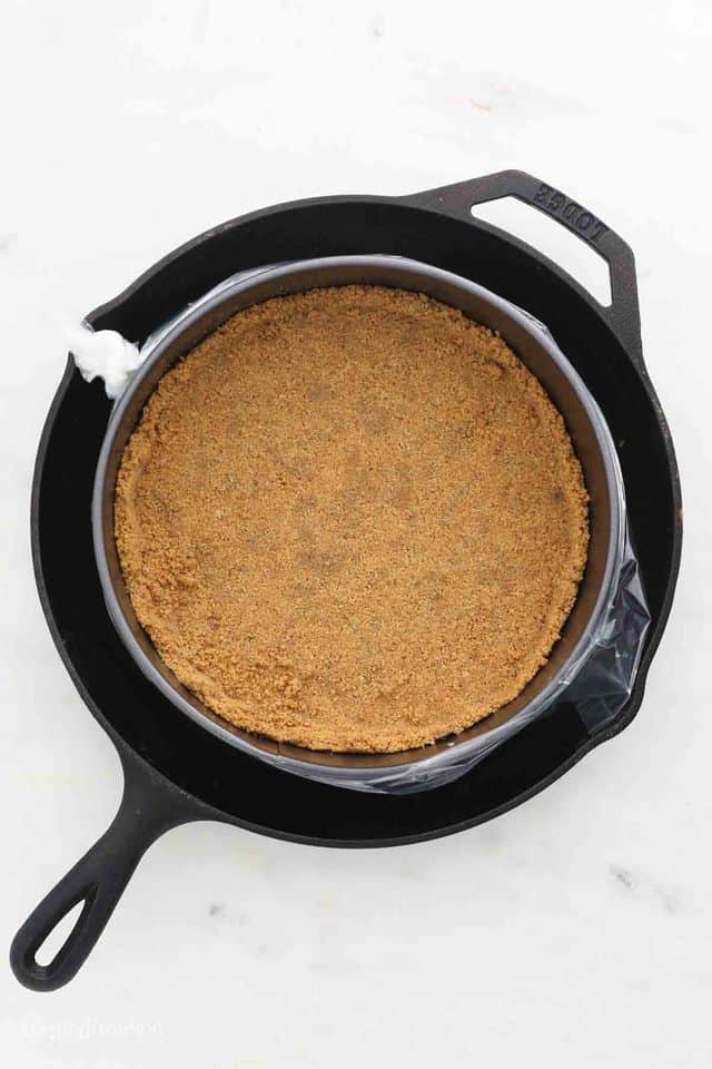 Graham cracker crust in a springform pan, inside a large cast iron pan.