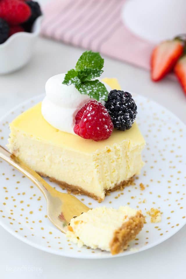 A slice of creamy homemade cheesecake topped with whipped cream and berries.