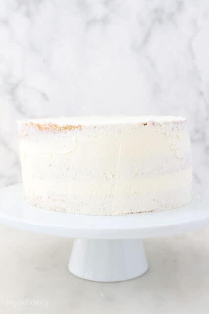 a white cake stand with a layer cake that is crumb coated