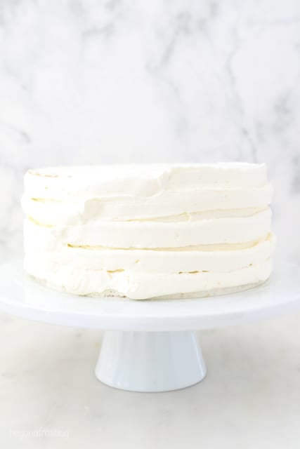 a white cake stand with a layer cake roughly frosted