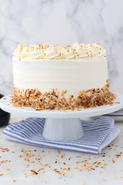 a white cake plate on a blue napkin. A frosted cake with toasted coconut