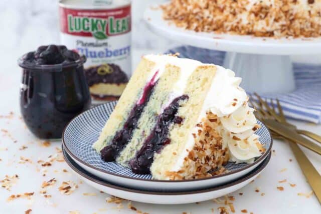 two stacked blue plates with a slice of cake, a cake stand and a jar of blueberry sauce