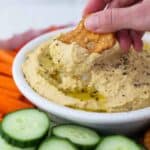 A Flat Pretzel Being Dipped into a Bowl of Homemade Hummus