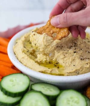 A Flat Pretzel Being Dipped into a Bowl of Homemade Hummus