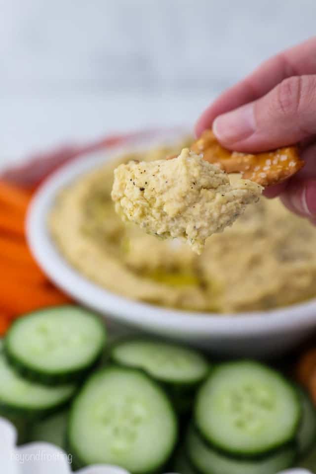 A Pretzel Hovering Over Cucumber Slices and Carrots with Hummus Dip on Top
