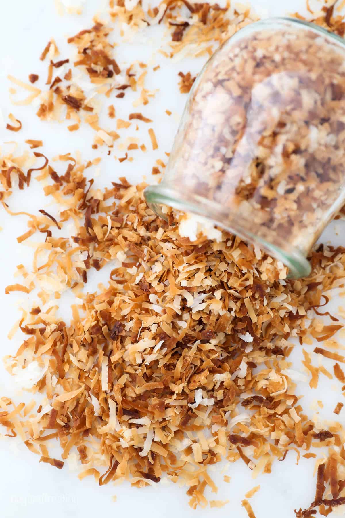 Toasted coconut spilling out on the counter from a glass jar