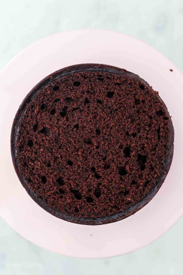 Bird's eye view of a layer of chocolate cake, flattened on top, sitting on a pink cake stand