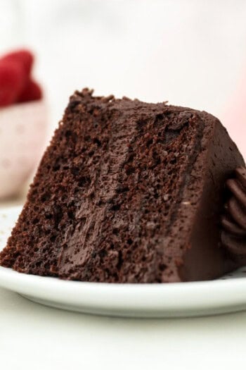 A slice of small chocolate cake topped with a swirl of chocolate buttercream laying on its side on a white plate.
