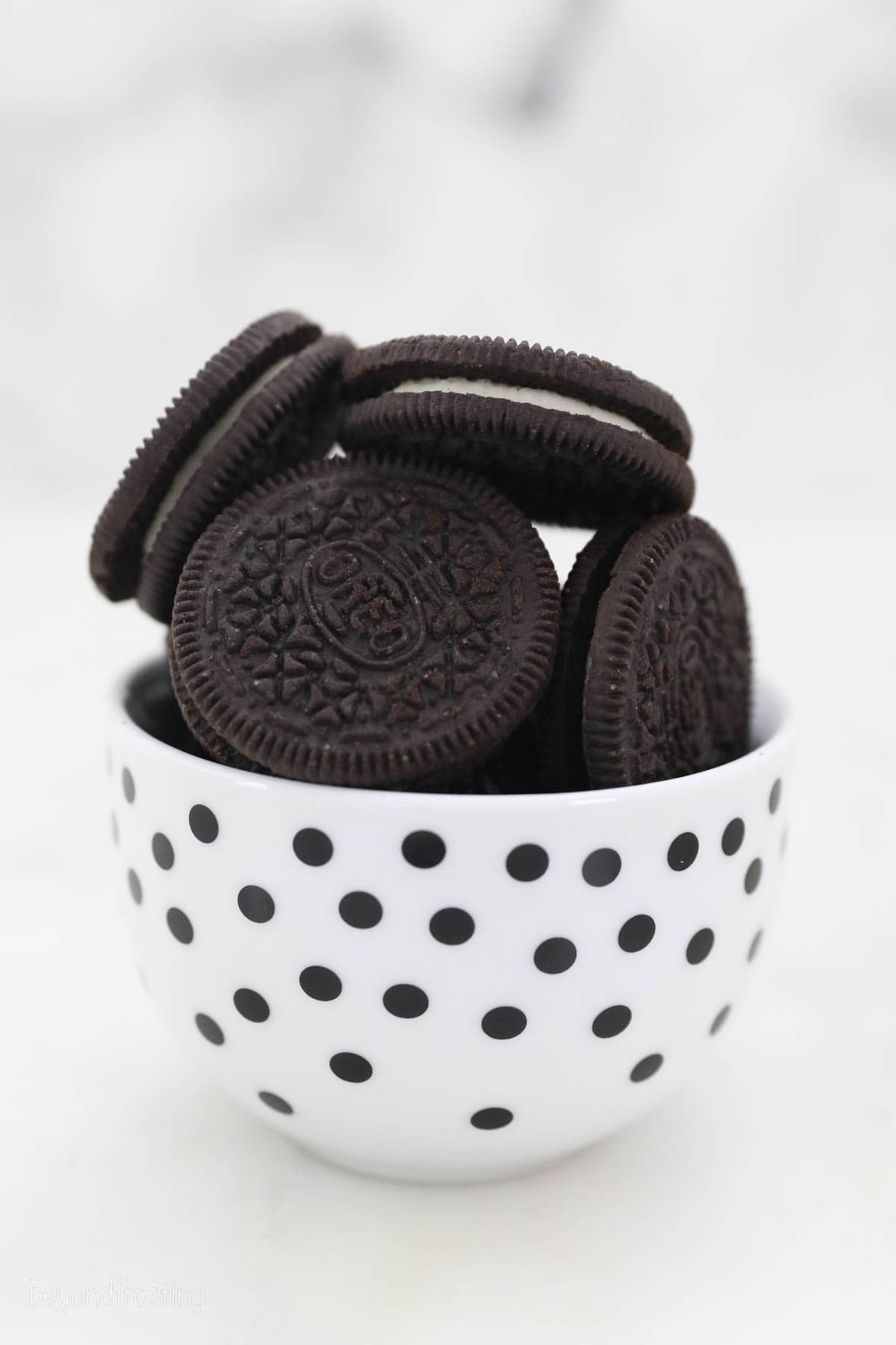 Oreo cookies stacked in a white bowl with black polka dots.