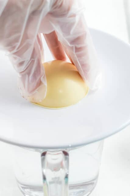 hands pressing a white chocolate sphere on a white plate
