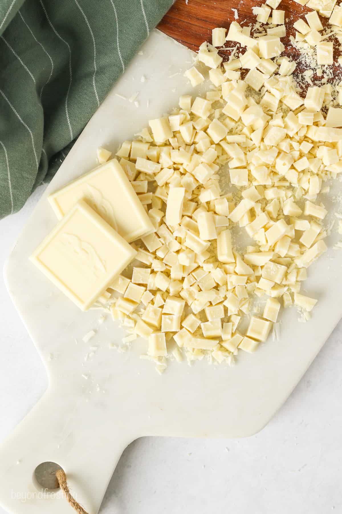 Overhead view of two white chocolate squares next to chopped white chocolate pieces on a cutting board.