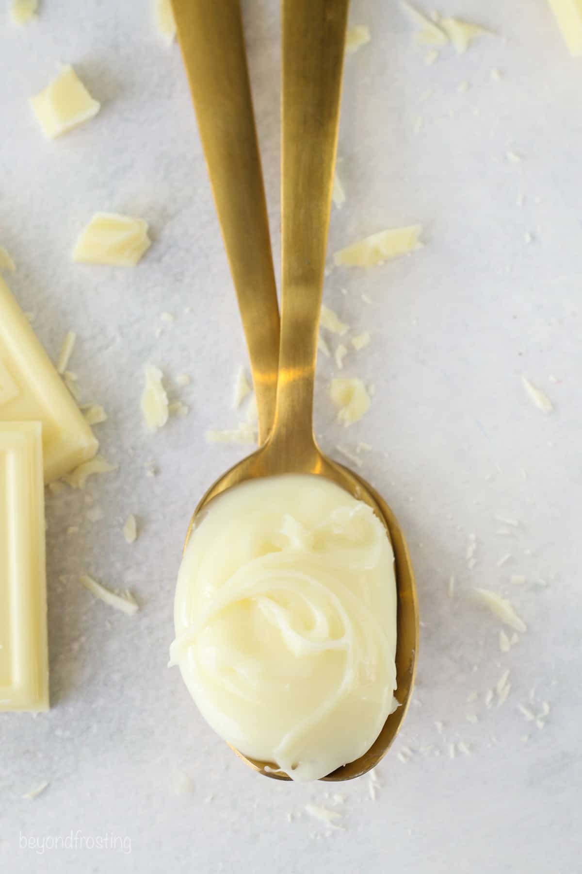 Overhead view of a spoonful of white chocolate ganache next to chopped white chocolate shavings.