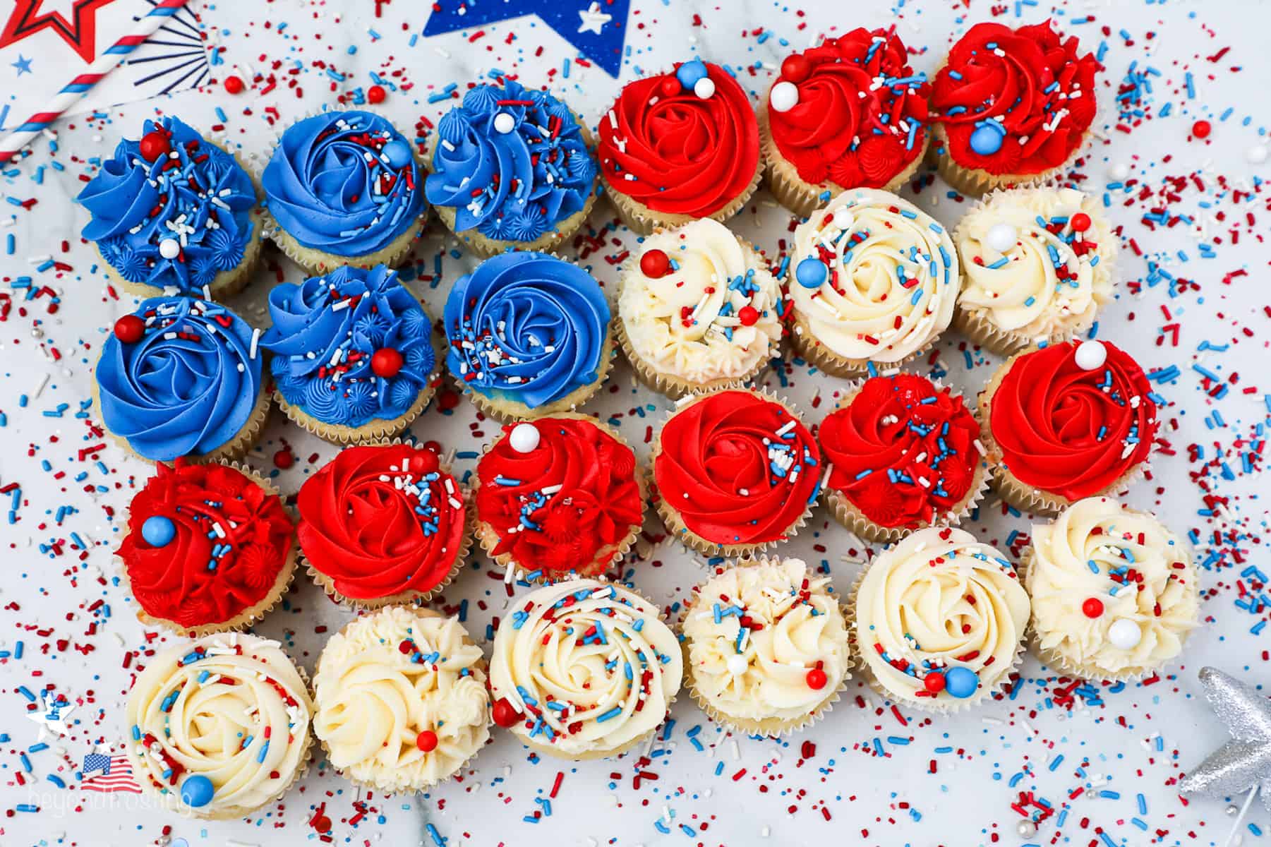 Overhead view of cupcakes decorated with red, white, and blue frosting and sprinkles arranged in the shape of an American flag.