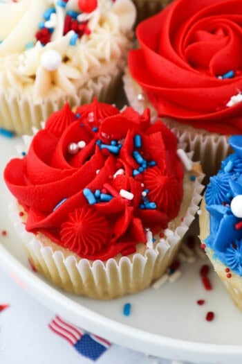 Assorted red, white, and blue frosted cupcakes decorated with sprinkles on a plate.