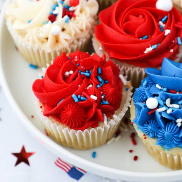 Assorted red, white, and blue frosted cupcakes decorated with sprinkles on a plate.