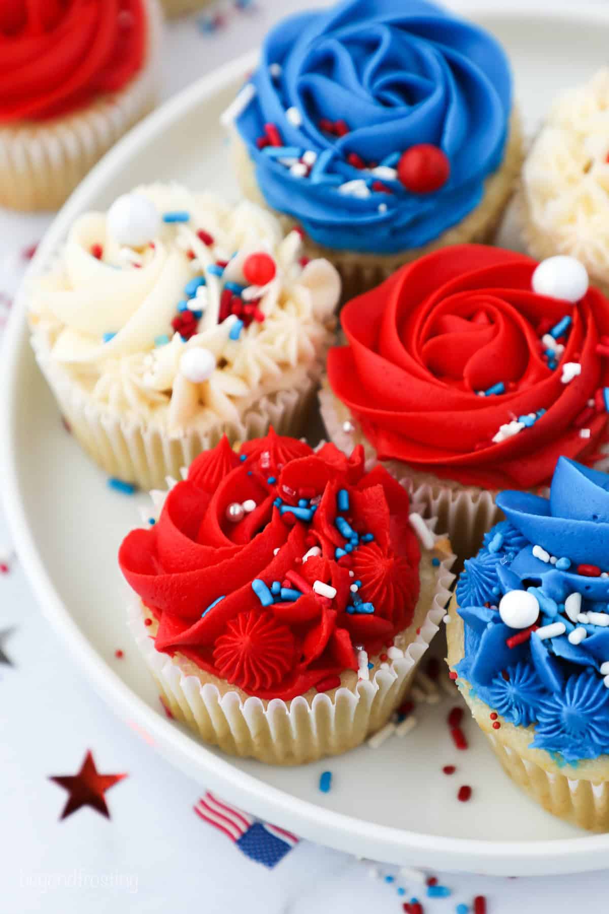 Assorted red, white, and blue frosted cupcakes decorated with sprinkles on a plate.