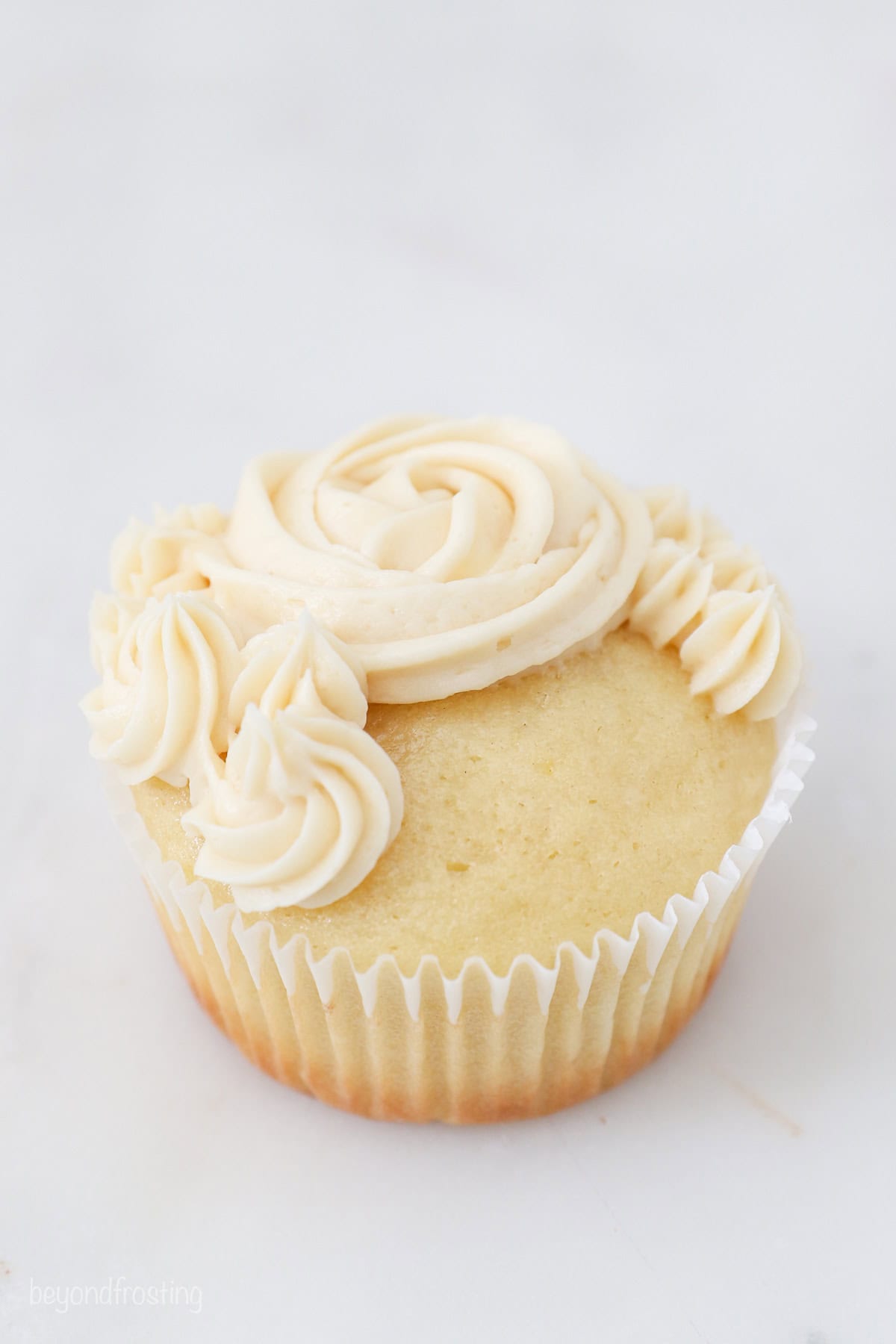 A cupcake partially frosted with vanilla frosting swirls and rosettes.