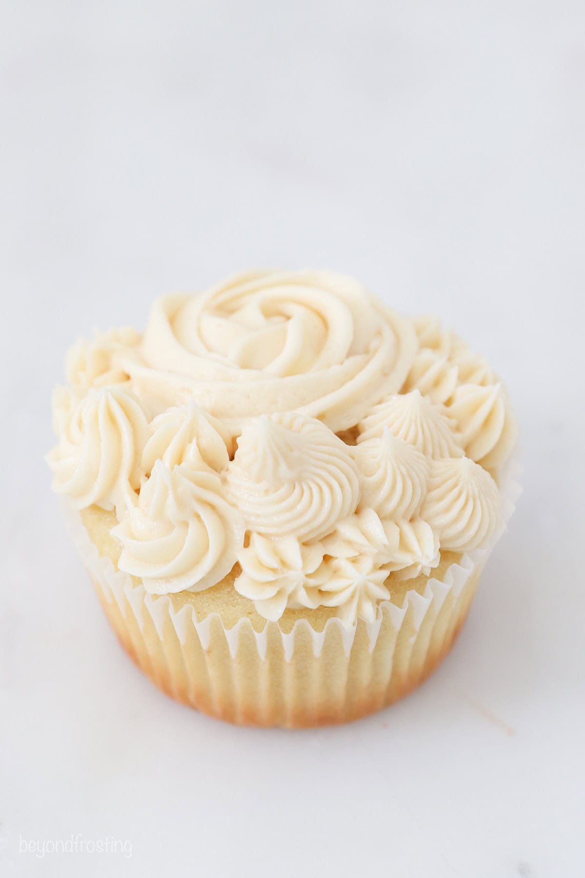 A cupcake frosted with various vanilla frosting swirls and rosettes.